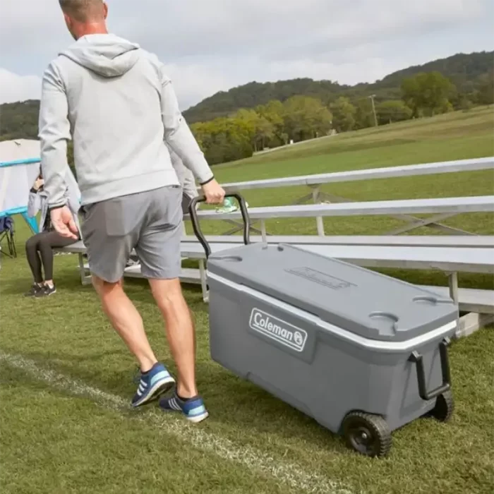 Hombre acarreando en campo de deportes una Conservadora Chest 100qt Con Ruedas Made In Usa - Rock Gray